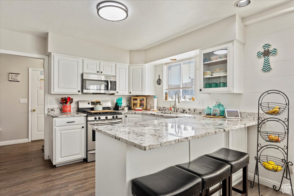 Kitchen featuring light stone countertops, white cabinetry, dark hardwood / wood-style floors, appliances with stainless steel finishes, and a breakfast bar