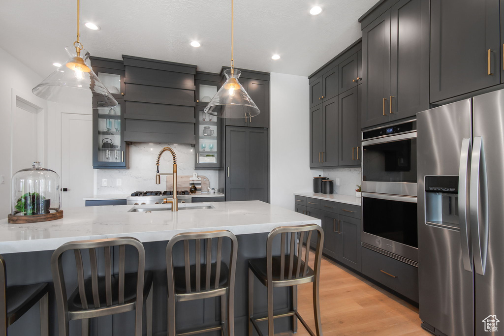 Kitchen with pendant lighting, a kitchen breakfast bar, appliances with stainless steel finishes, and light hardwood / wood-style flooring