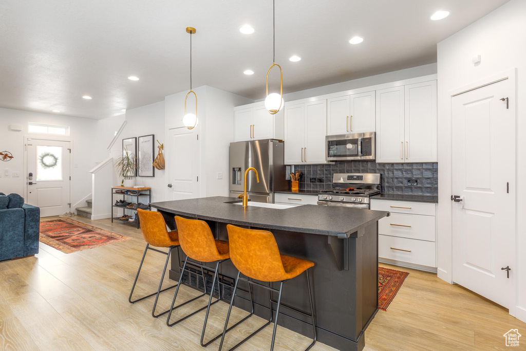Kitchen featuring an island with sink, white cabinets, appliances with stainless steel finishes, light hardwood / wood-style flooring, and a kitchen bar
