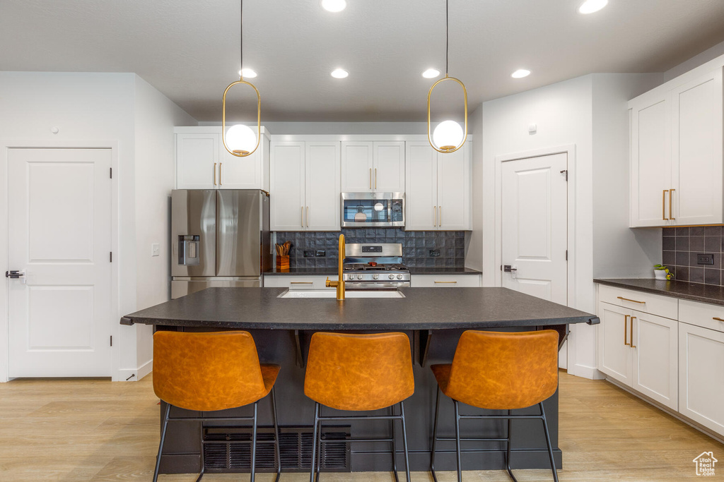 Kitchen featuring an island with sink, stainless steel appliances, and decorative light fixtures