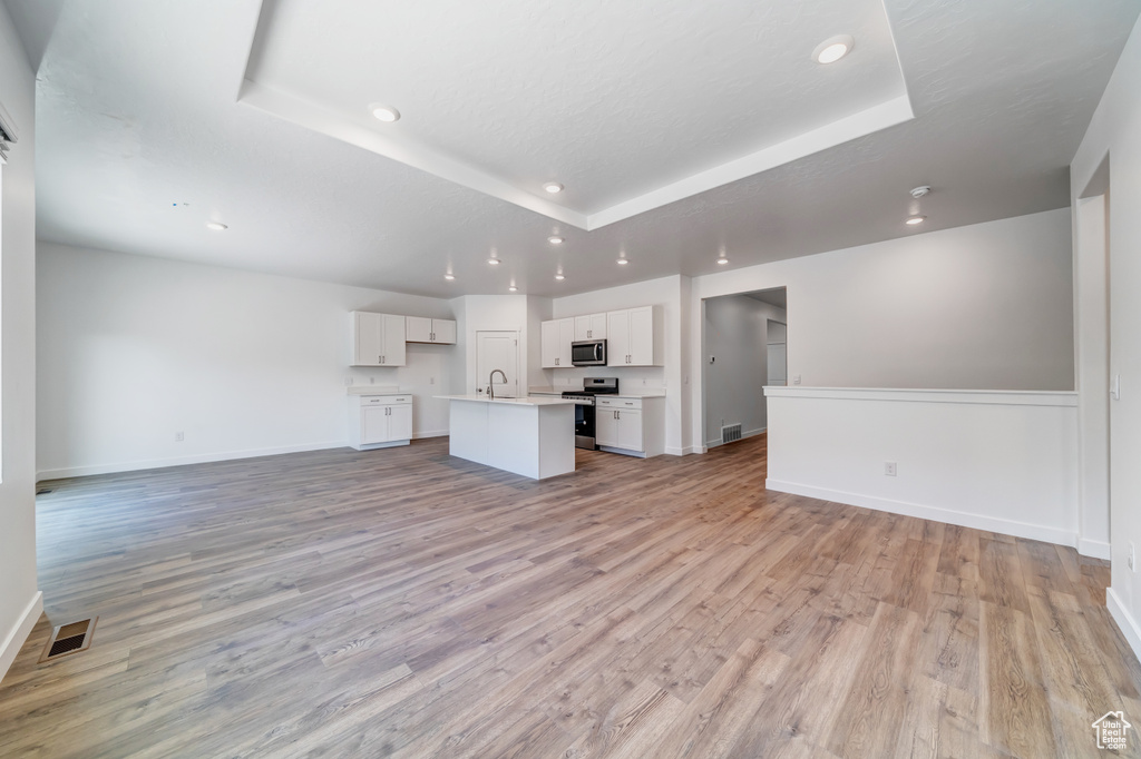 Unfurnished living room with a tray ceiling, sink, and light hardwood / wood-style flooring