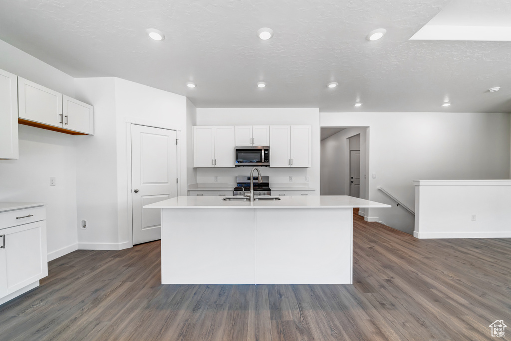 Kitchen featuring a center island with sink, white cabinetry, appliances with stainless steel finishes, dark hardwood / wood-style floors, and sink