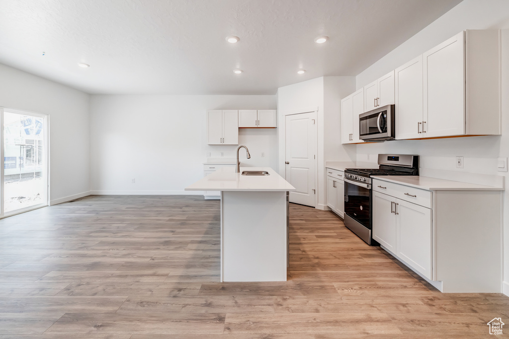 Kitchen featuring white cabinets, a center island with sink, light hardwood / wood-style flooring, and stainless steel appliances