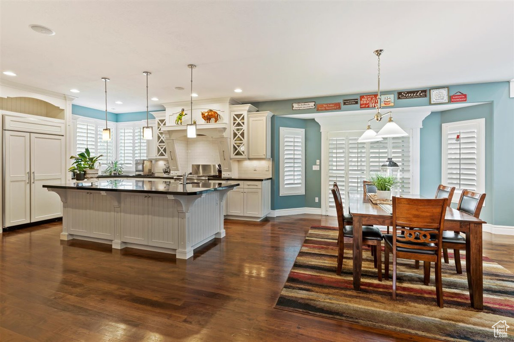 Kitchen with an island with sink, dark hardwood / wood-style floors, tasteful backsplash, and decorative light fixtures