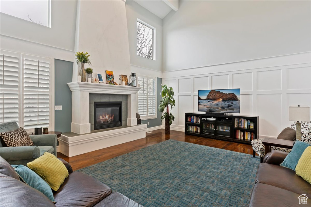 Living room with a high ceiling, a tiled fireplace, dark wood-type flooring, and a wealth of natural light