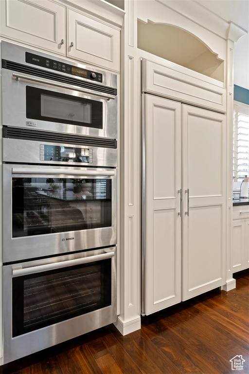 Kitchen with stainless steel double oven, white cabinets, dark wood-type flooring, and sink
