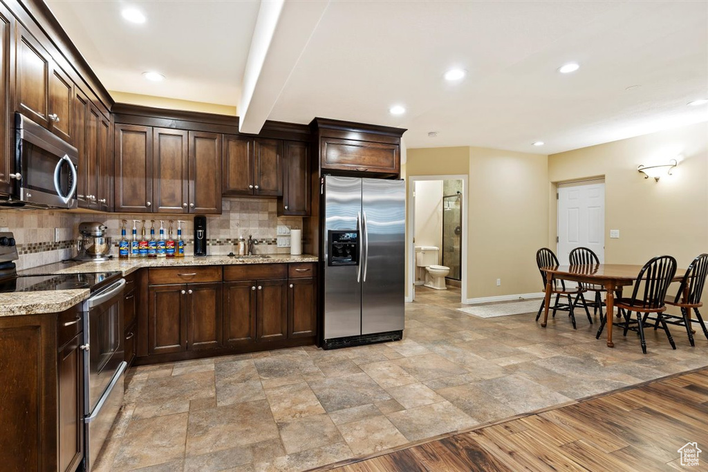 Kitchen featuring light tile floors, light stone counters, dark brown cabinets, appliances with stainless steel finishes, and tasteful backsplash