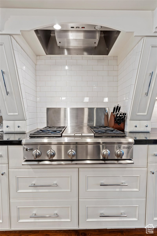 Kitchen with white cabinets, backsplash, stainless steel gas cooktop, and wall chimney range hood
