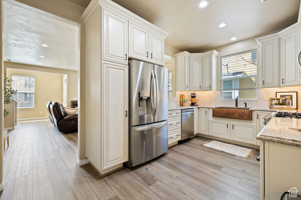Kitchen with white cabinetry, light hardwood / wood-style floors, appliances with stainless steel finishes, and a wealth of natural light