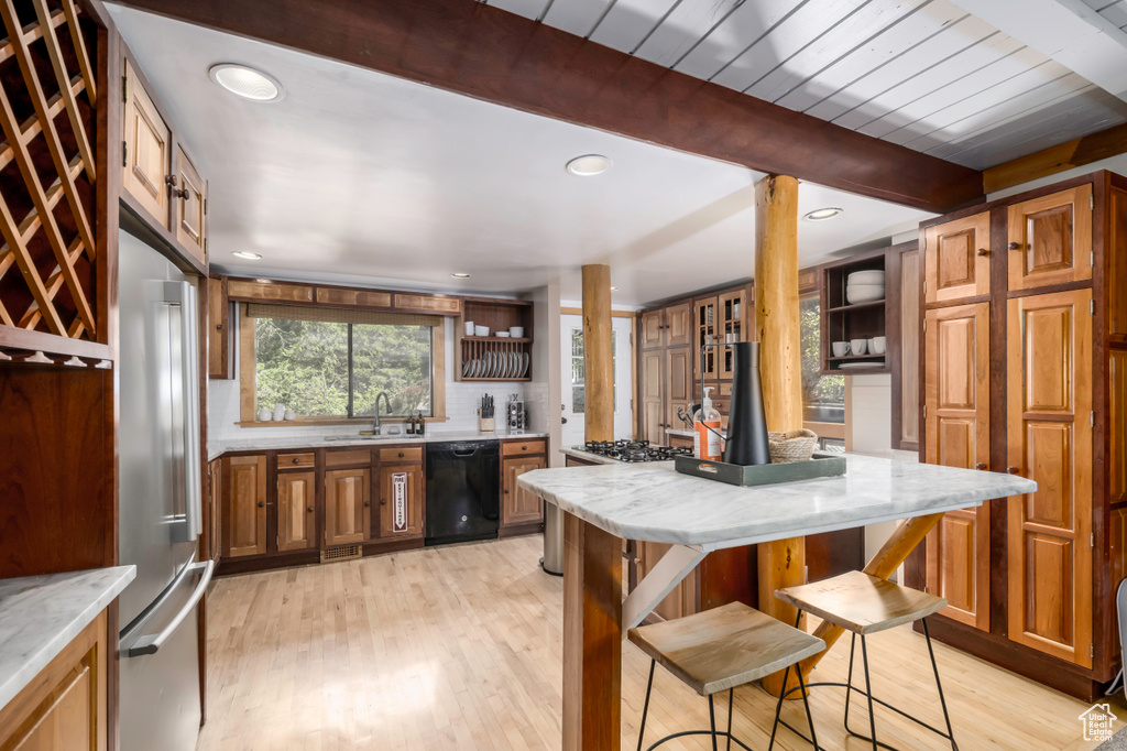 Kitchen featuring high end fridge, beamed ceiling, a breakfast bar, light hardwood / wood-style flooring, and black dishwasher
