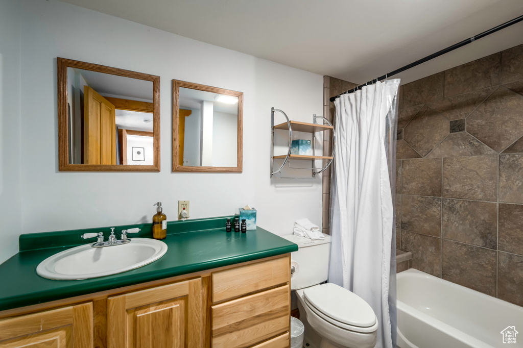 Full bathroom with toilet, shower / bathtub combination with curtain, and vanity with extensive cabinet space