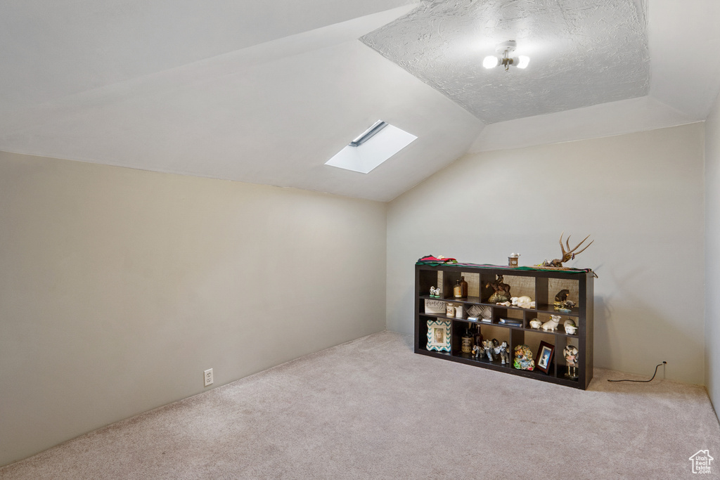 Additional living space featuring light colored carpet, lofted ceiling with skylight, and a textured ceiling