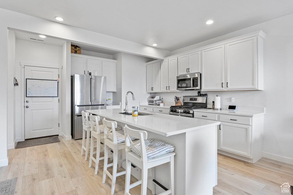 Kitchen featuring sink, appliances with stainless steel finishes, a center island with sink, white cabinetry, and light wood-type flooring
