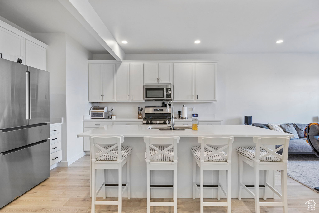 Kitchen featuring white cabinets, appliances with stainless steel finishes, a breakfast bar area, and light hardwood / wood-style flooring