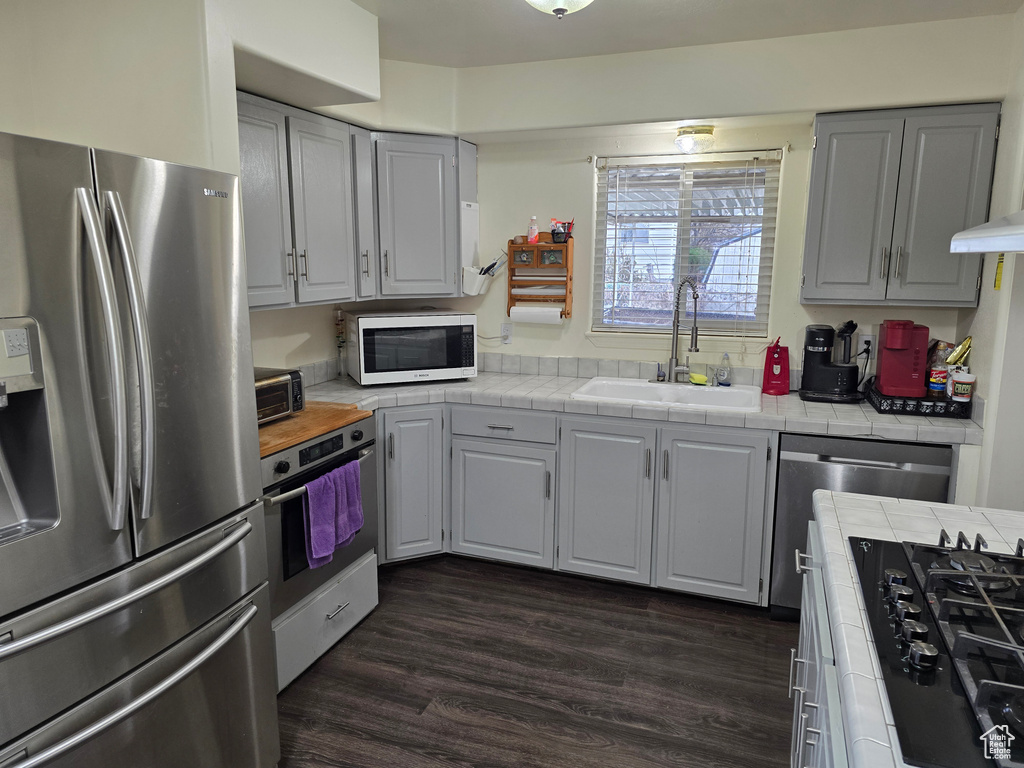 Kitchen featuring gray cabinets, dark wood-type flooring, appliances with stainless steel finishes, tile counters, and sink