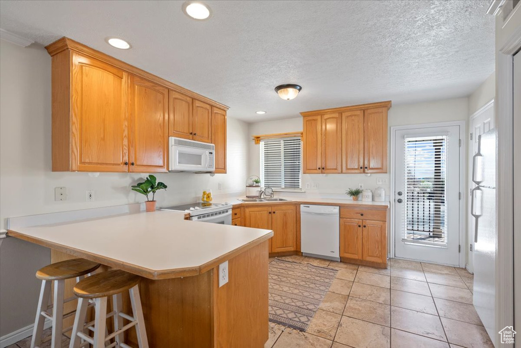 Kitchen with a kitchen breakfast bar, white appliances, light tile flooring, kitchen peninsula, and sink