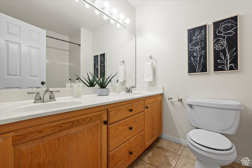Bathroom featuring vanity with extensive cabinet space, toilet, double sink, and tile flooring