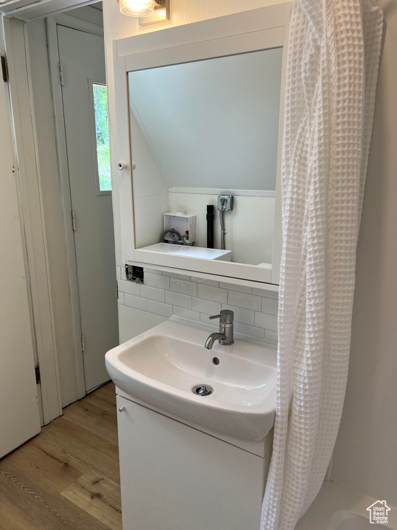 Bathroom with hardwood / wood-style flooring, vanity, lofted ceiling, backsplash, and shower / tub combo with curtain