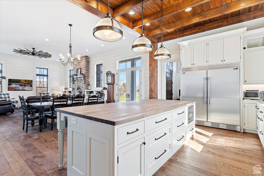 Kitchen with pendant lighting, a kitchen island, white cabinets, built in fridge, and light wood-type flooring