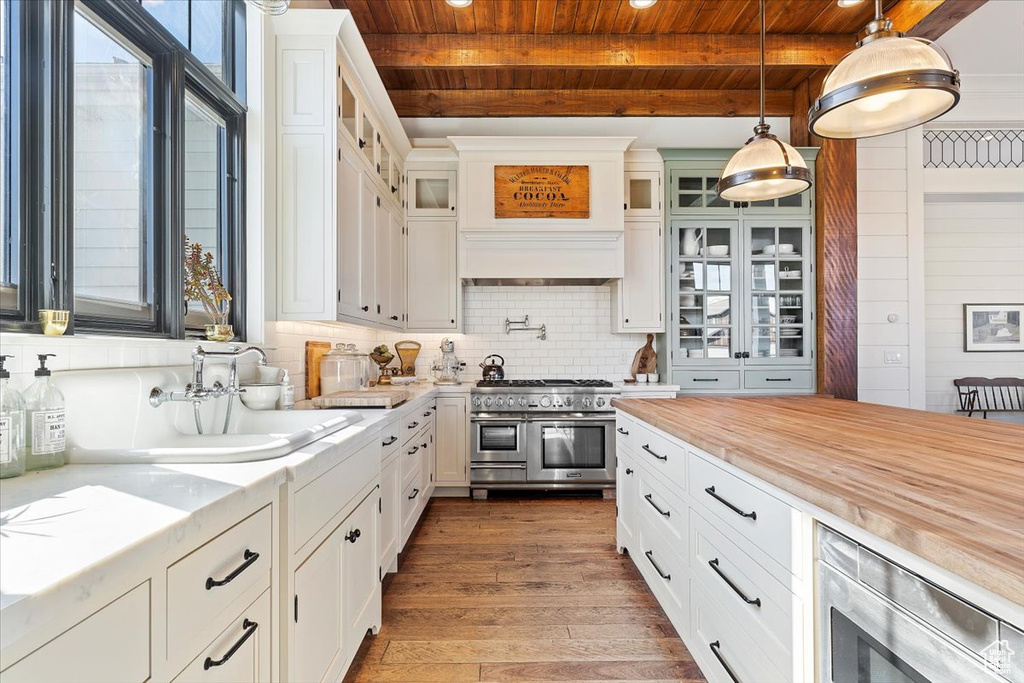 Kitchen with double oven range, beamed ceiling, light hardwood / wood-style flooring, white cabinetry, and hanging light fixtures