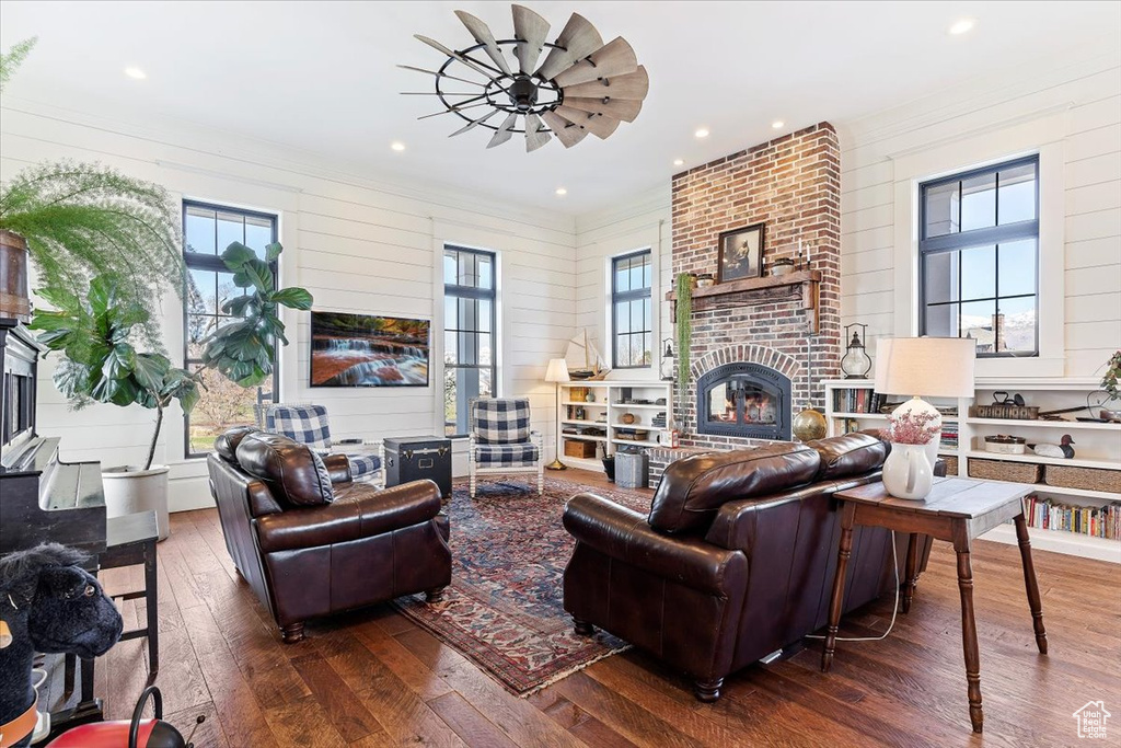 Living room featuring ceiling fan, brick wall, dark wood-type flooring, and a fireplace