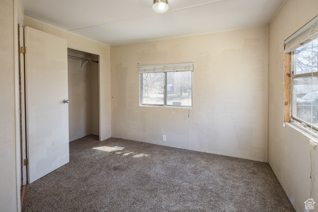 Unfurnished bedroom featuring dark colored carpet, a closet, and multiple windows