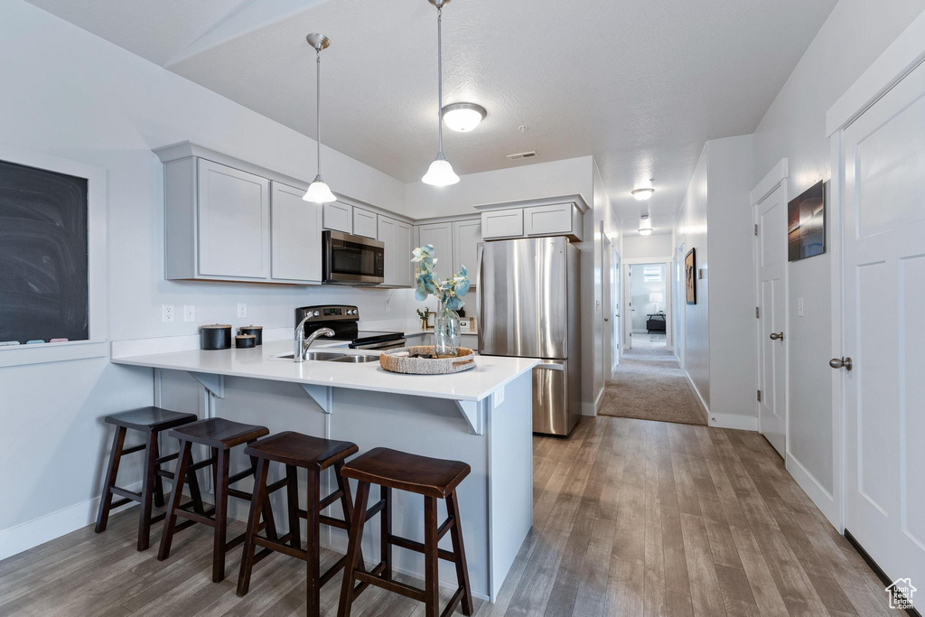 Kitchen featuring stainless steel appliances, decorative light fixtures, a kitchen bar, light wood-type flooring, and sink
