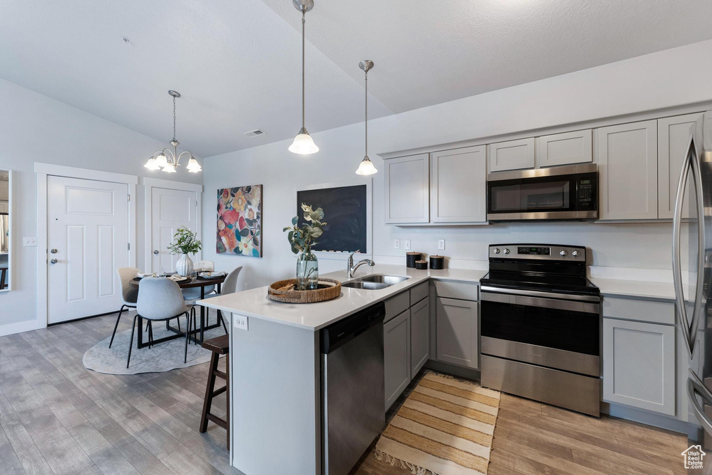 Kitchen featuring pendant lighting, light hardwood / wood-style floors, a notable chandelier, appliances with stainless steel finishes, and lofted ceiling