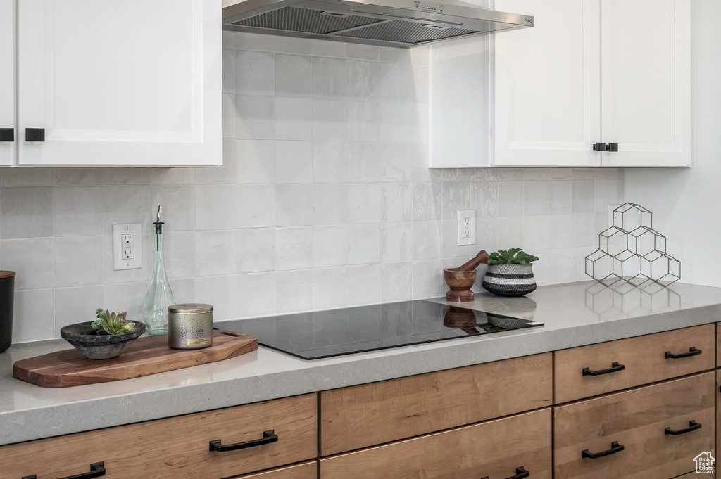 Kitchen featuring backsplash, wall chimney range hood, and white cabinetry