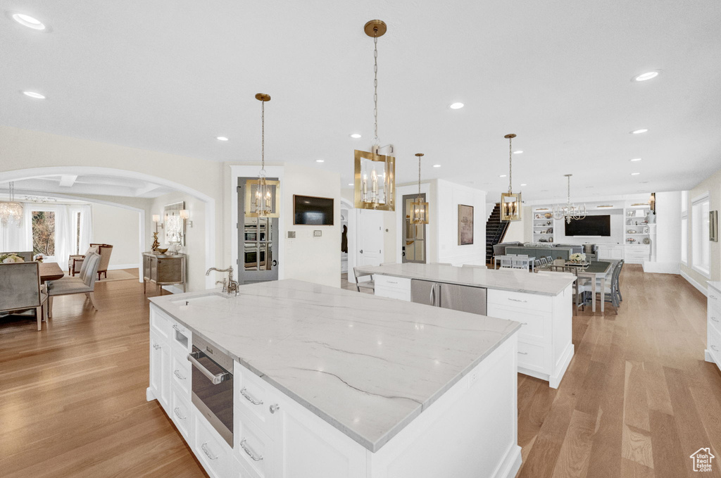 Kitchen with sink, white cabinets, light hardwood / wood-style flooring, light stone countertops, and a center island