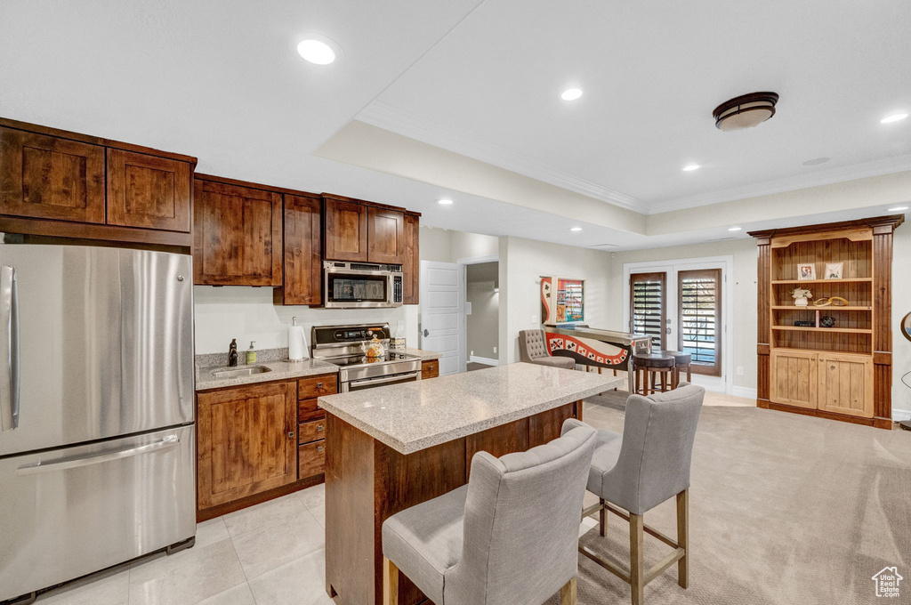 Kitchen featuring a kitchen breakfast bar, appliances with stainless steel finishes, a raised ceiling, and light colored carpet