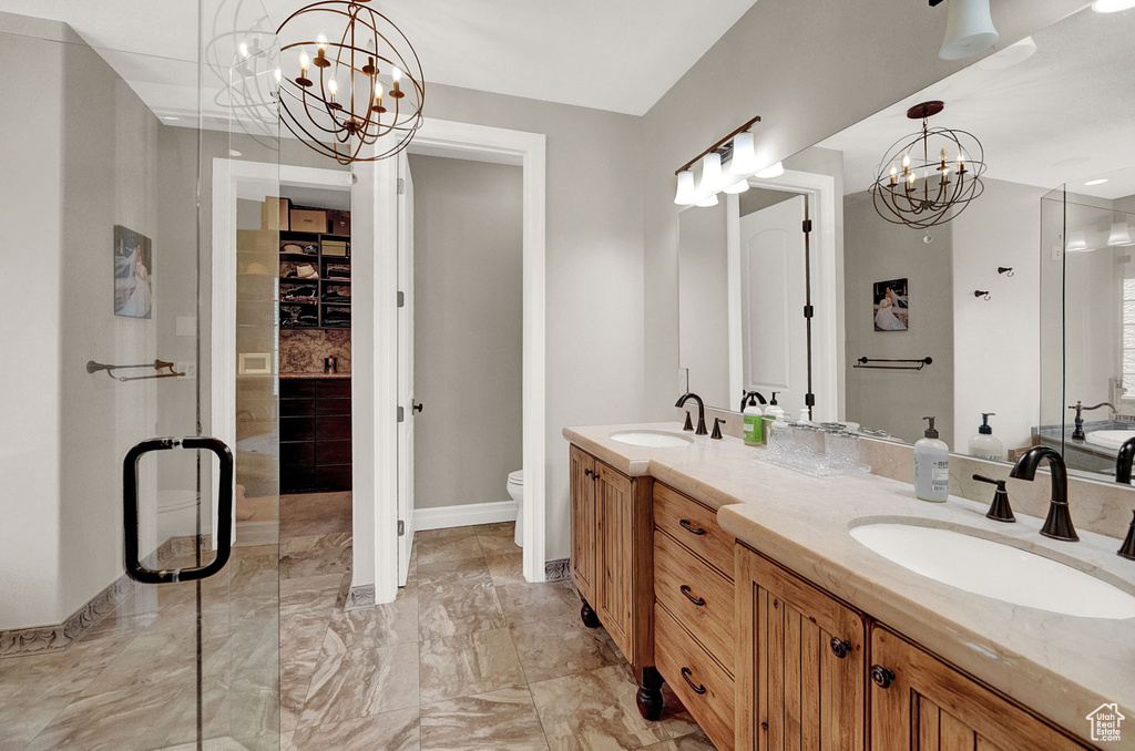 Bathroom featuring toilet, vanity with extensive cabinet space, tile flooring, dual sinks, and an inviting chandelier