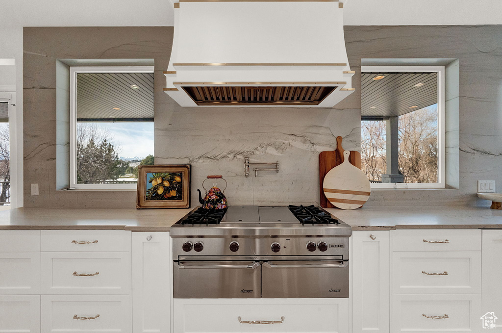 Kitchen featuring white cabinetry, custom exhaust hood, tasteful backsplash, and high end stove