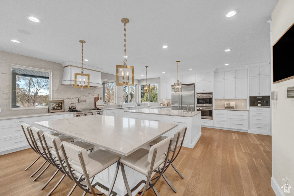 Kitchen featuring white cabinets, a center island with sink, light wood-type flooring, and stainless steel appliances