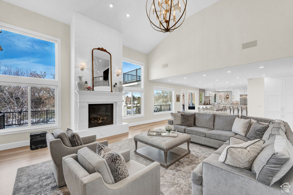 Living room with a fireplace, an inviting chandelier, high vaulted ceiling, light hardwood / wood-style flooring, and a wealth of natural light