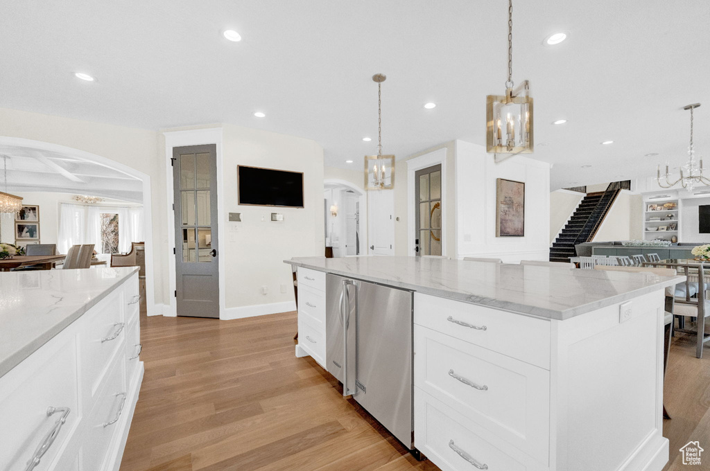 Kitchen with pendant lighting, light wood-type flooring, light stone countertops, white cabinetry, and a center island