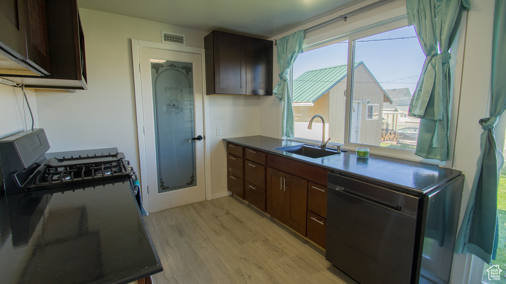Kitchen featuring dark brown cabinetry, black dishwasher, light wood-type flooring, and sink