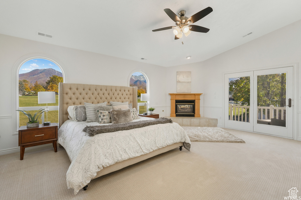 Bedroom with a tile fireplace, ceiling fan, multiple windows, and access to outside
