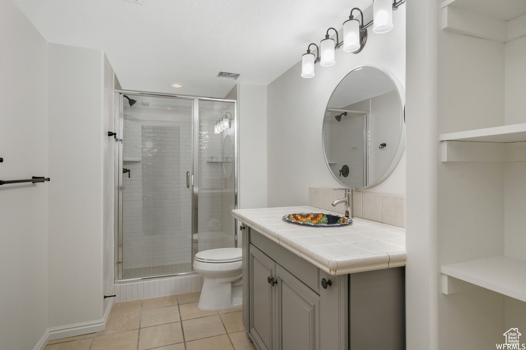 Bathroom featuring toilet, a shower with door, large vanity, and tile flooring