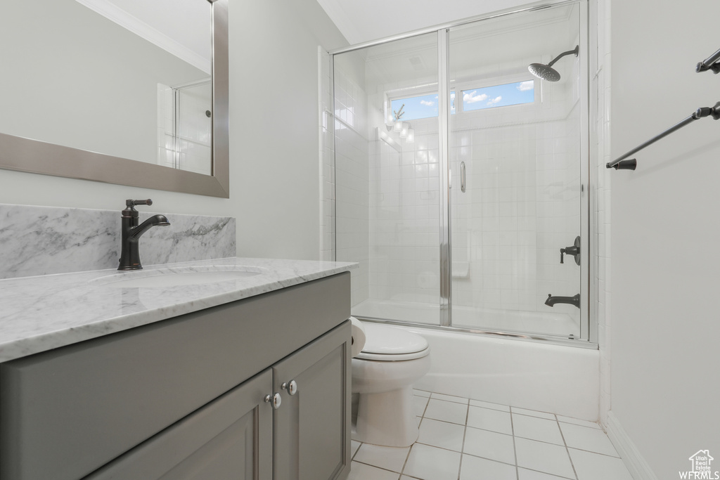 Full bathroom featuring toilet, shower / bath combination with glass door, vanity with extensive cabinet space, ornamental molding, and tile floors