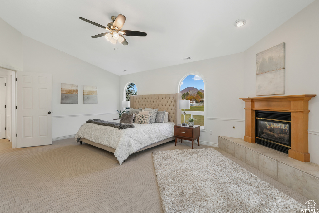 Carpeted bedroom featuring a tiled fireplace, ceiling fan, and vaulted ceiling