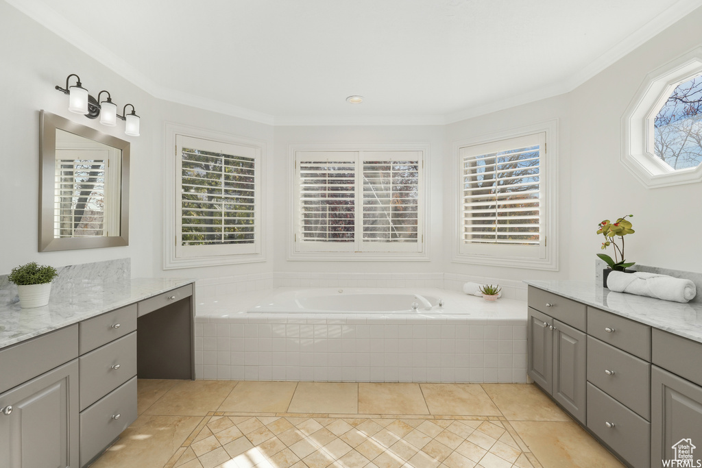 Bathroom featuring tiled bath, plenty of natural light, vanity with extensive cabinet space, and ornamental molding