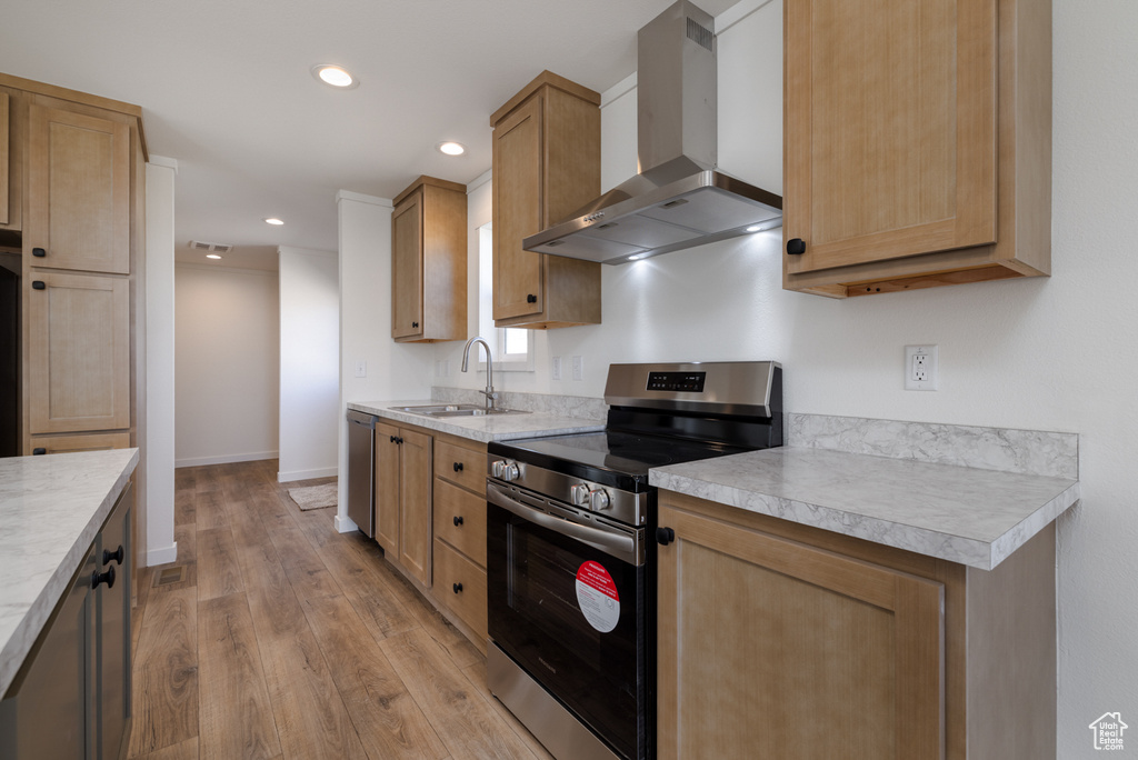 Kitchen featuring light hardwood / wood-style flooring, wall chimney exhaust hood, appliances with stainless steel finishes, and sink