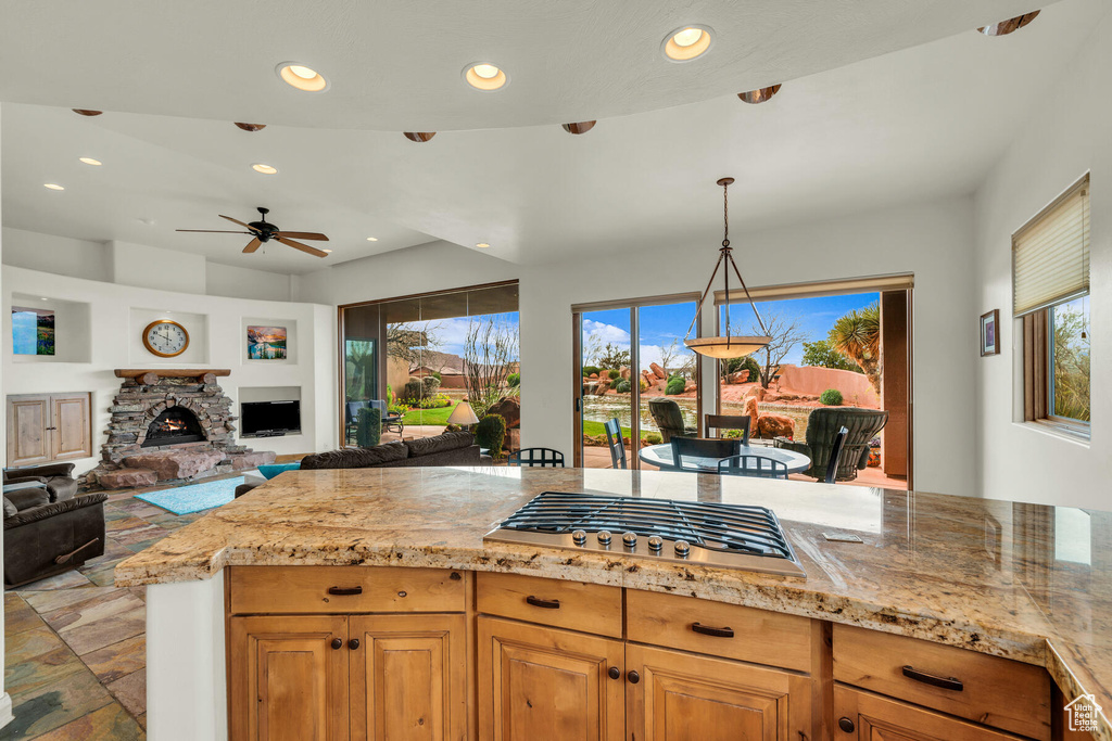 Kitchen featuring light stone countertops, hanging light fixtures, stainless steel gas cooktop, ceiling fan, and a fireplace