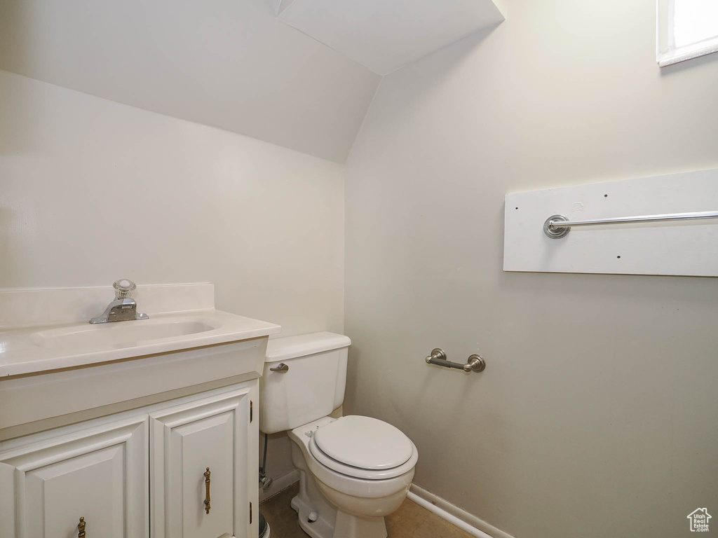 Bathroom featuring toilet, vanity, lofted ceiling, and tile flooring