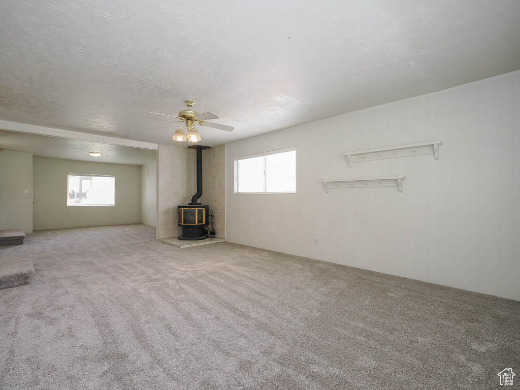 Unfurnished living room featuring light carpet, a textured ceiling, ceiling fan, and a wood stove