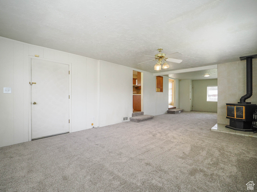 Unfurnished living room with light carpet, a textured ceiling, ceiling fan, and a wood stove