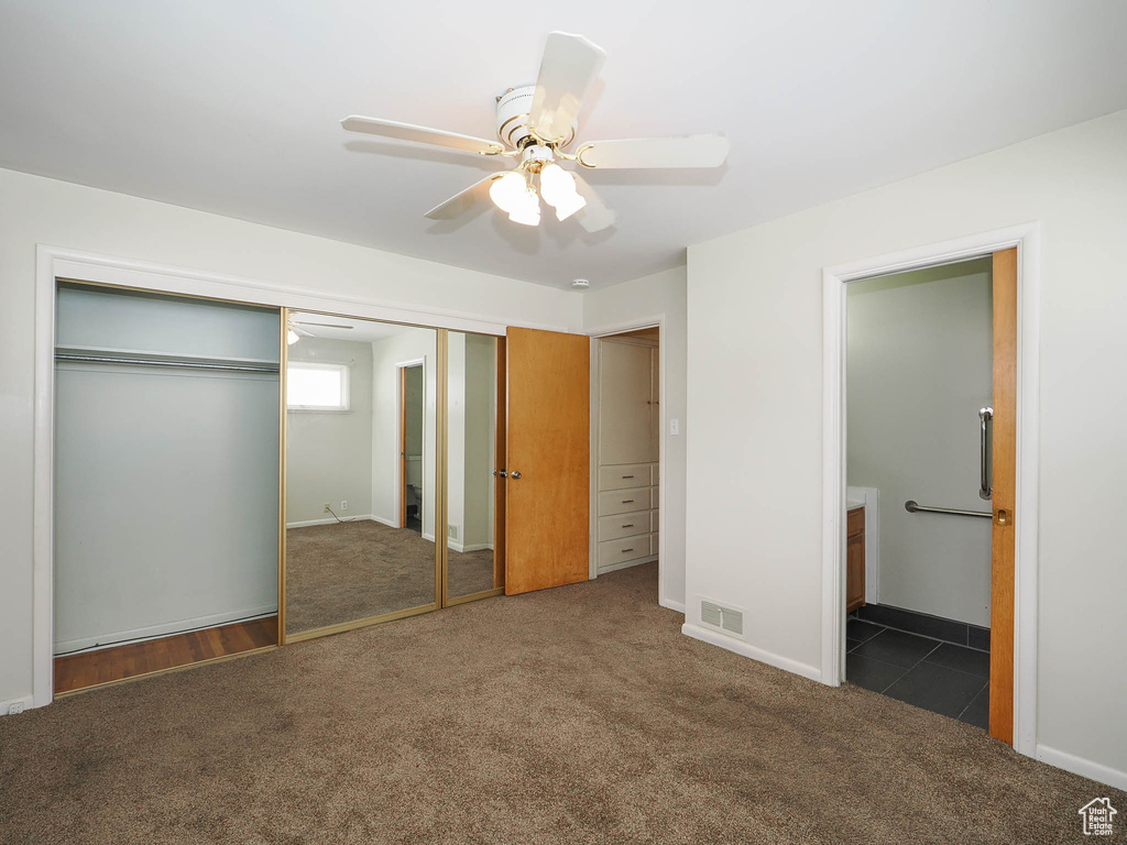 Unfurnished bedroom featuring ensuite bath, a closet, ceiling fan, and dark carpet