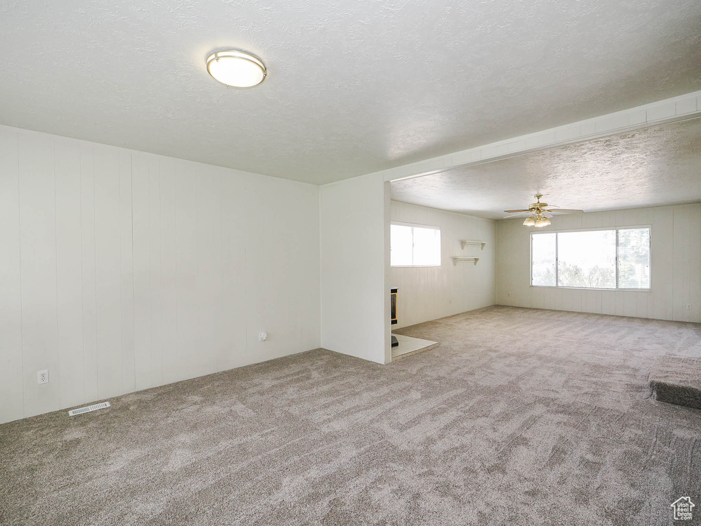 Carpeted spare room featuring plenty of natural light, ceiling fan, and a textured ceiling