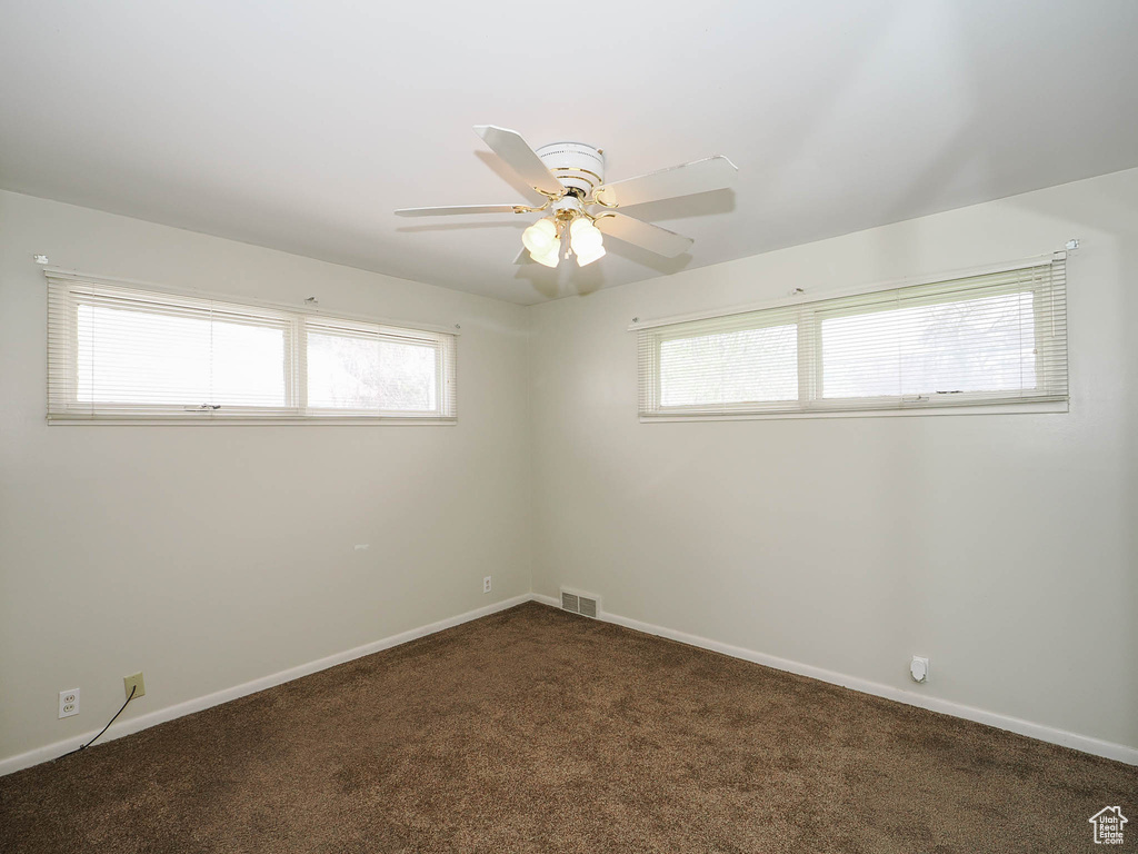 Carpeted empty room featuring plenty of natural light and ceiling fan